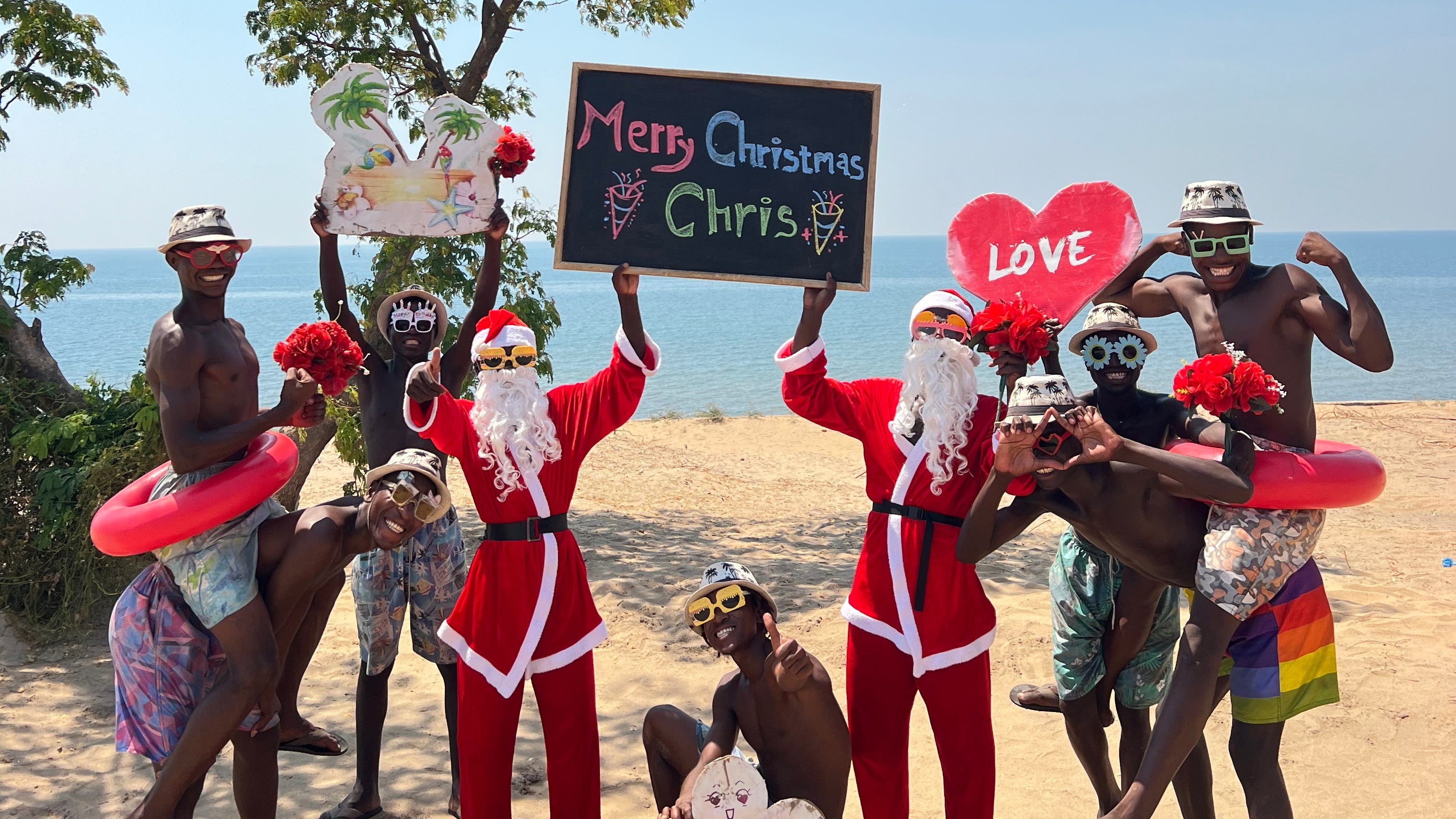Group of people in Christmas-themed costumes on a beach with a clear blue sky.