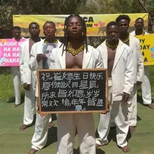 Group of people in white outfits with a person holding a sign outdoors. nad make greetings video from Africa